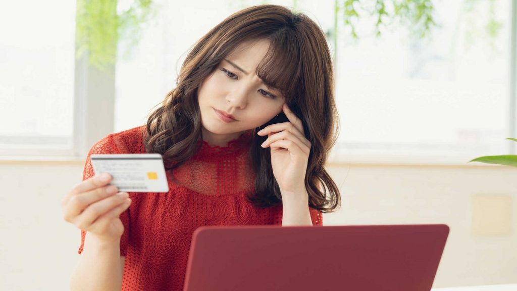 Mulher segurando um cartão de crédito na frente do computador com um semblante de duvida como se quisesse entender como funciona o cartão do empréstimo consignado