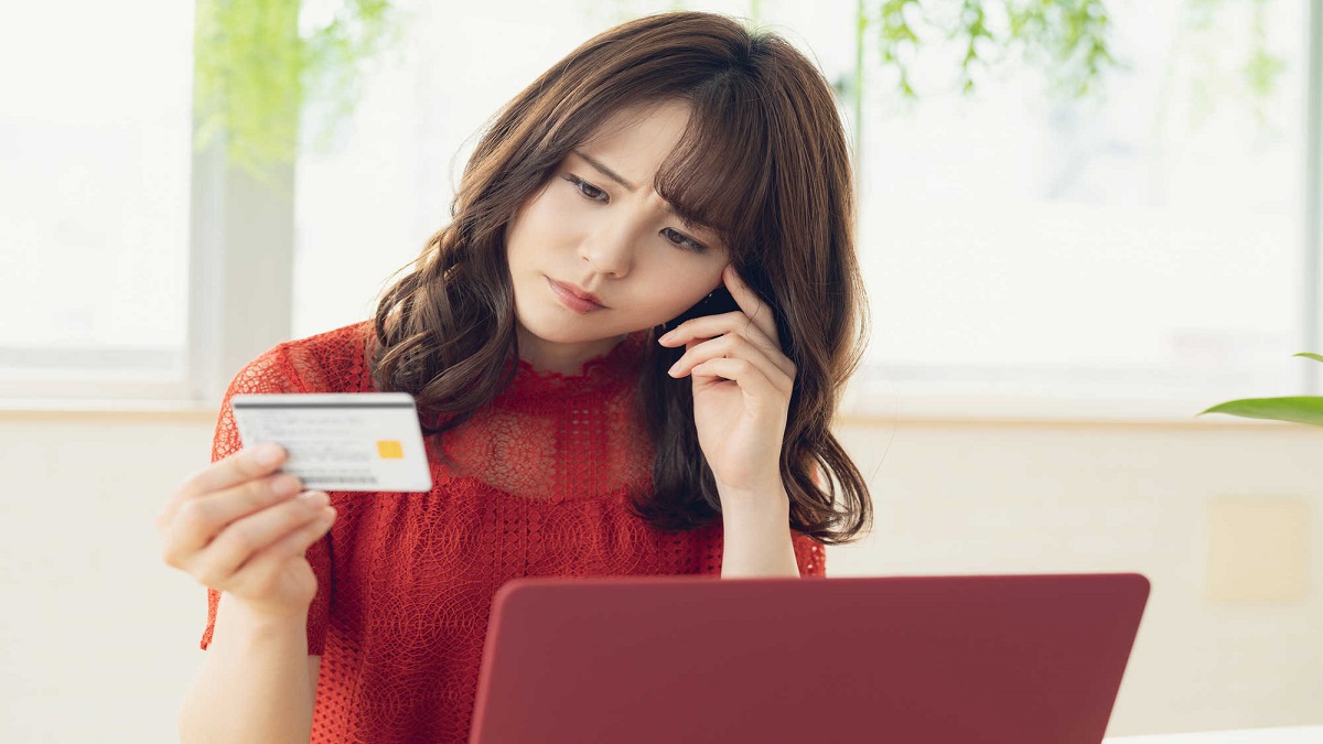 Mulher segurando um cartão de crédito na frente do computador com um semblante de duvida como se quisesse entender como funciona o cartão do empréstimo consignado