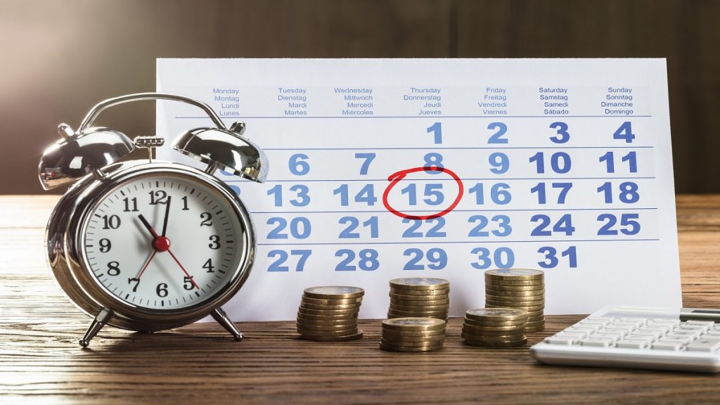 uma mesa com despertador moedas e um calendário com o dia quinze circulado, sugerindo que quase metade dos brasileiros buscaram sobre empréstimo em agosto.